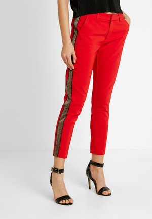 Røde slim-fit bukser med en glitrende sort sidestribe, båret med sorte høje hælede sandaletter med ankelrem og en sort top.