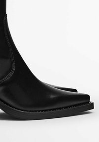 Stivaletti neri in pelle con punta affilata, texture liscia e tacco ampio e piatto. Presentano dettagli di cucitura minimi lungo la suola.
