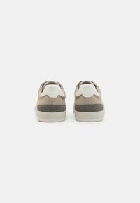Beige vászon felsőrészű, szürke velúr sarkú és fehér kiegészítőkkel rendelkező sneakers. Alacsony szárú kivitelű, texturált nyelve van. Látható gumitalpa.