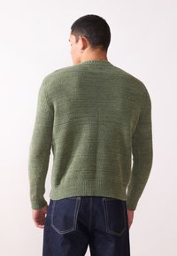 Green textured sweater with long sleeves and ribbed hem, paired with dark denim jeans. No notable patterns or hardware visible.