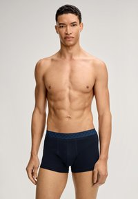 Tummansinisenä, sileästä puuvillasekoitteesta valmistetut boxerit, joissa on kuvioitu, sinisävyinen vyötärönauha. Edessä näkyy aukko.