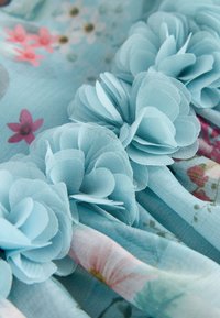 Tissu bleu clair avec des fleurs en couches translucides cousues, avec un motif imprimé de petites fleurs roses et blanches.