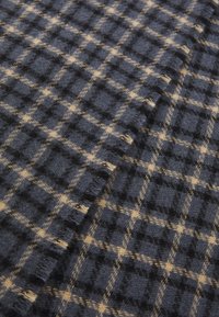 Navy and beige plaid fabric, made of soft wool. Features a textured surface with check patterns and fringed edges, overlapping slightly.