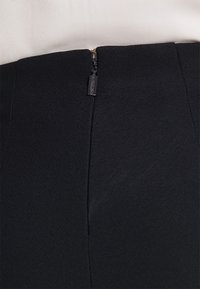 Svart tygplagg med en slät textur, med en liten dragkedja på baksidan. Inga synliga mönster eller accenter.