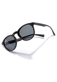 Black sunglasses with large round lenses and a matte finish. Slim arms with branding detail, designed with a minimalist shape.
