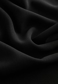 Crna tkanina s glatkom teksturom, koja sadrži mekane nabore i suptilne detalje uzorka, prikazujući duboku, uniformnu boju i elegantno drapiranje.