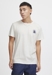 Kamyšinė t-shirta off-white spalvos, trumpomis rankovėmis, su mažuoju mėlynu grafiniu logotipu kairėje krūtinės pusėje. Lygus audinys, paprasto apvalaus kaklo dizainas.