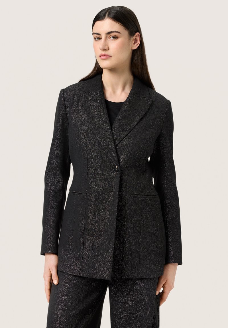 Fekete zakó texturált anyagból, finom fémes részletekkel, csúcsos hajtókákkal és két elülső zsebbel a szabott illeszkedés érdekében.