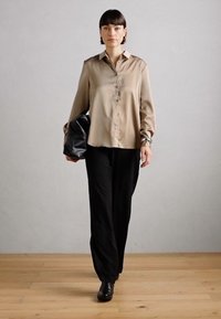 Light brown satin button-up shirt with a collar, paired with black loose-fitting pants and a black textured bag, worn with black shoes.