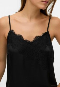 Czarna satynowa koszulka na cienkich ramiączkach, z koronkowym wykończeniem wzdłuż dekoltu i na ramionach, gładka w dotyku, o luźnym kroju.