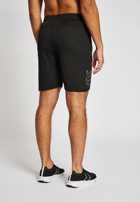Shorts de sport noirs avec une ceinture à cordon de serrage, un design ajusté et des motifs en chevron blancs distinctifs sur les côtés.