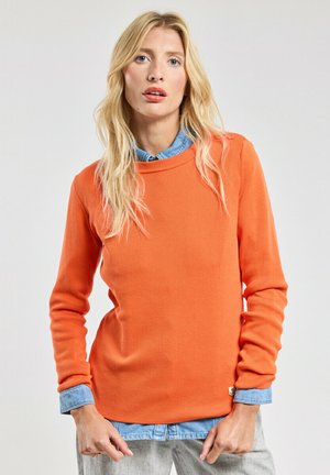 Pull orange à côtes avec un col rond, présentant de longues manches et des poignets de chemise en denim visibles en dessous. Conception simple et décontractée.