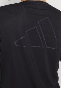 Schwarzes Sportshirt mit strukturiertem Stoff, das auf der Rückseite ein dezentes Logo in Dunkelgrau aufweist, mit rundem Ausschnitt und kurzen Ärmeln.