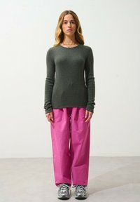 Groen gebreid sweater met lange mouwen, gecombineerd met losse roze broek. Model draagt grijze sneakers en staat tegen een neutrale achtergrond.