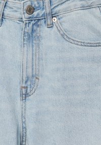 Jean en denim bleu clair en gros plan montrant la poche avant, la passoire de ceinture, le bouton en métal et les détails de couture.