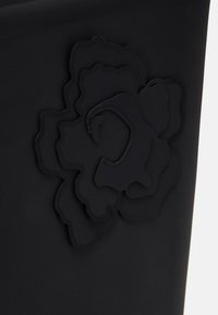 Surface en caoutchouc noir présentant un design floral en relief et en couches avec des détails cousus ressemblant à un motif de pétales de fleurs stylisé.