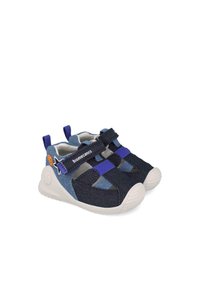 Zapatos infantiles de denim azul y oscuro con correas de velcro, tela texturizada, suela de goma y acento de logo en el lateral.