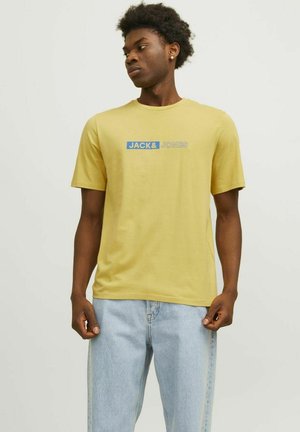 Camiseta de algodón amarilla de manga corta, con un logo azul y gris que dice "JACK&JONES" en el pecho. Corte casual.
