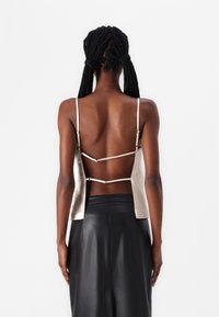Back view of a beige satin camisole with thin straps, featuring an open back design and adjustable hardware details. Paired with a black leather skirt.