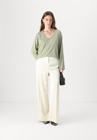 Ljusgrön långärmad topp med V-ringning och avslappnad passform, ihop med höga, vida byxor i krämfärg och en liten svart handväska.