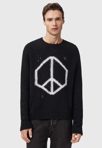 Pulover negru tricotat cu un mare simbol alb al păcii. Designul include detalii distresate vizibile și manșete și tiv cu rigle.