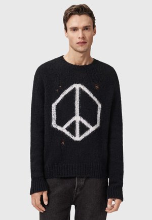 Pull en tricot noir avec un grand symbole de paix blanc. Le design présente des détails usés visibles ainsi que des poignets et un ourlet côtelés.