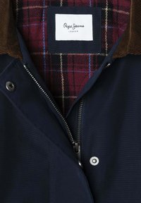 Jūrų laivyno striukė su ruduojo velveto apykakle, sidabro užtrauktuku ir raudonais languotais pamušalu su mėlynais ir kreminiu akcentais. Matoma Pepe Jeans etiketė.