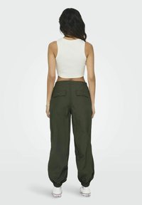 Afgeknotte witte tanktop gecombineerd met loszittende, donkergroene cargo-broek met twee achterzakken en elastische boorden. Witte sneakers maken de look af.