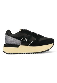 Sneaker nera con materiali in suede e pelle, caratterizzata da un accento di glitter grigio sul tallone, una robusta suola color crema e lacci neri.