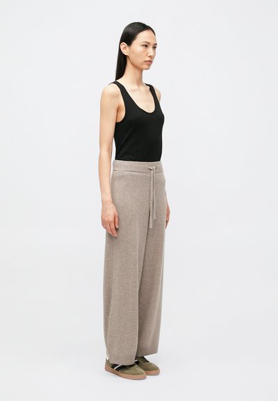 Lahtised beežid kootud püksid paeltega vöökohas, mida kombineeritakse kehaühtlaselt sobiva musta tank-topi ja oliivroheliste tossudega.