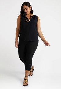 Top nero senza maniche con scollatura a V, abbinato a leggings neri e sandali flat con un accento dorato. Tessuto morbido e vestibilità attillata.