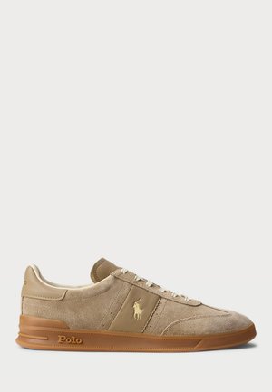 Baskets en daim tan avec une finition texturée, lacets blancs et semelle en caoutchouc tan. Présente un emblème doré et une marque "Polo" sur le côté.