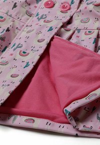 Imperméable rose avec un motif de lamas et de cactus. L'intérieur est doublé de rose uni et possède deux boutons roses à l'avant.