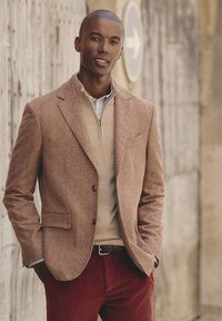 Blazer a Doppio Impuntura marrone su un maglione beige a zip quarti, abbinato a pantaloni in velluto a coste rossi. Presenta dettagli con bottoni e polsini a righe.