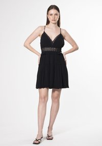 Schwarzes Minikleid mit Spaghettiträgern, Spitzenbesatz und mehrlagigem Design. Aus leichtem Stoff gefertigt, mit Rüschendetails am Saum.