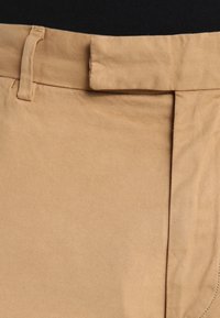 Beige tygbyxor med en slät struktur, med en plan framsida, bältesöglor och en diskret sidoficka.