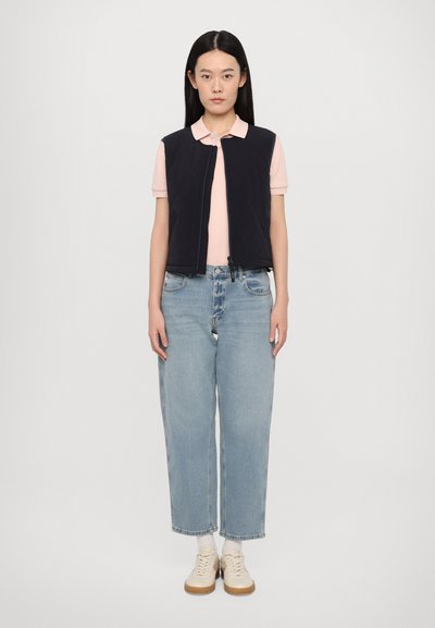 Navy quilted vest over a light pink polo, paired with high-waisted light blue jeans and beige sneakers. Features a zipper closure.