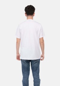 T-shirt bianca in cotone con maniche corte, collo tondo e vestibilità rilassata, abbinata a jeans di denim blu chiaro.