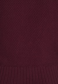Pull en tricot bordeaux présentant un motif en point texturé avec un ourlet côtelé. Le matériau semble doux et chaud. Aucun accent supplémentaire visible.