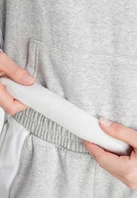 Un sweat-shirt gris avec une douce doublure en polaire blanche. Il possède une poche kangourou et une taille élastique pour plus de confort. Gros plan sur la main et les détails du tissu.