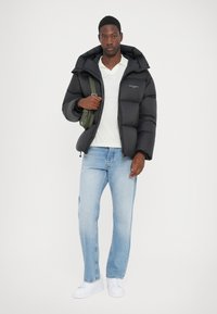 Sort pufferjakke med hætte, med quiltede sektioner og et subtilt logo. Parret med lyseblå denimjeans og hvide sneakers.
