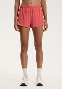 Pink athletic shorts with an elastic waistband, a loose cut, and smooth fabric. Worn with white socks and light sneakers.