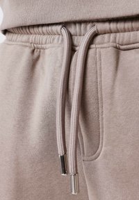 Light beige sweatshirt material close-up, featuring a ribbed neckline, elastic waistband, and drawstrings with metal tips.
