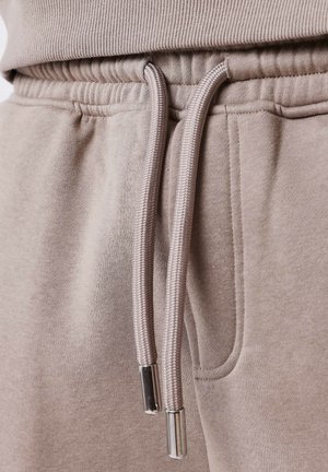 Primer plano de un material de sudadera beige claro, con un cuello acanalado, cinturilla elástica y cordones con puntas de metal.