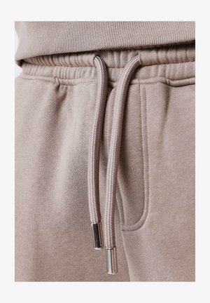 Primer plano de un material de sudadera beige claro, con un cuello acanalado, cinturilla elástica y cordones con puntas de metal.