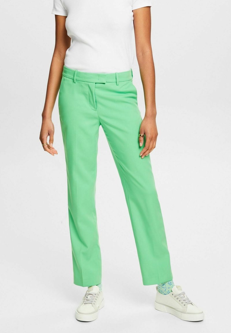 Green trousers with a tailored fit, lightweight fabric, flat front, and belt loops, paired with white sneakers and patterned socks.