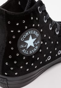 Svart sammet hög-top sneaker med silvernitar, runda öglor och en cirkulär logopatch med stjärndesign.