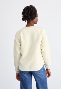Pullover in pile color crema con finitura testurizzata, maniche raglan, orlo arrotondato e vestibilità casual, abbinato a jeans in denim blu.