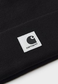 Black knitted beanie with a textured ribbed pattern. Features a white rectangular label with a black logo and brand name "carhartt."
