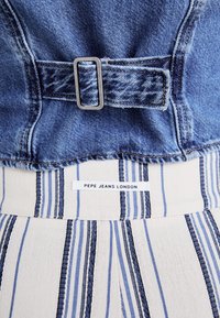 Modra denim bluzo z srebrno pravokotno zaponko in belim spodnjim delom iz tkanine, ki ima vertikalne modre črte. Na etiketi piše "PEPE JEANS LONDON."